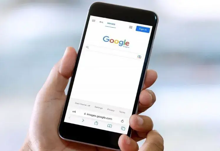 A hand holds a phone displaying the Google search page.